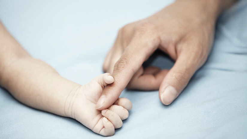 Barnhand håller i fingret på vuxenhand